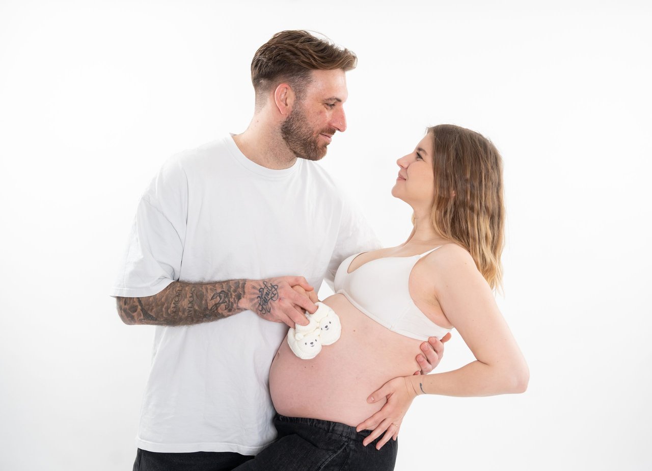 Babybauch-Shooting: Paar stehend mit Babyschuhchen, quer – Photography Ruel, Ebreichsdorf