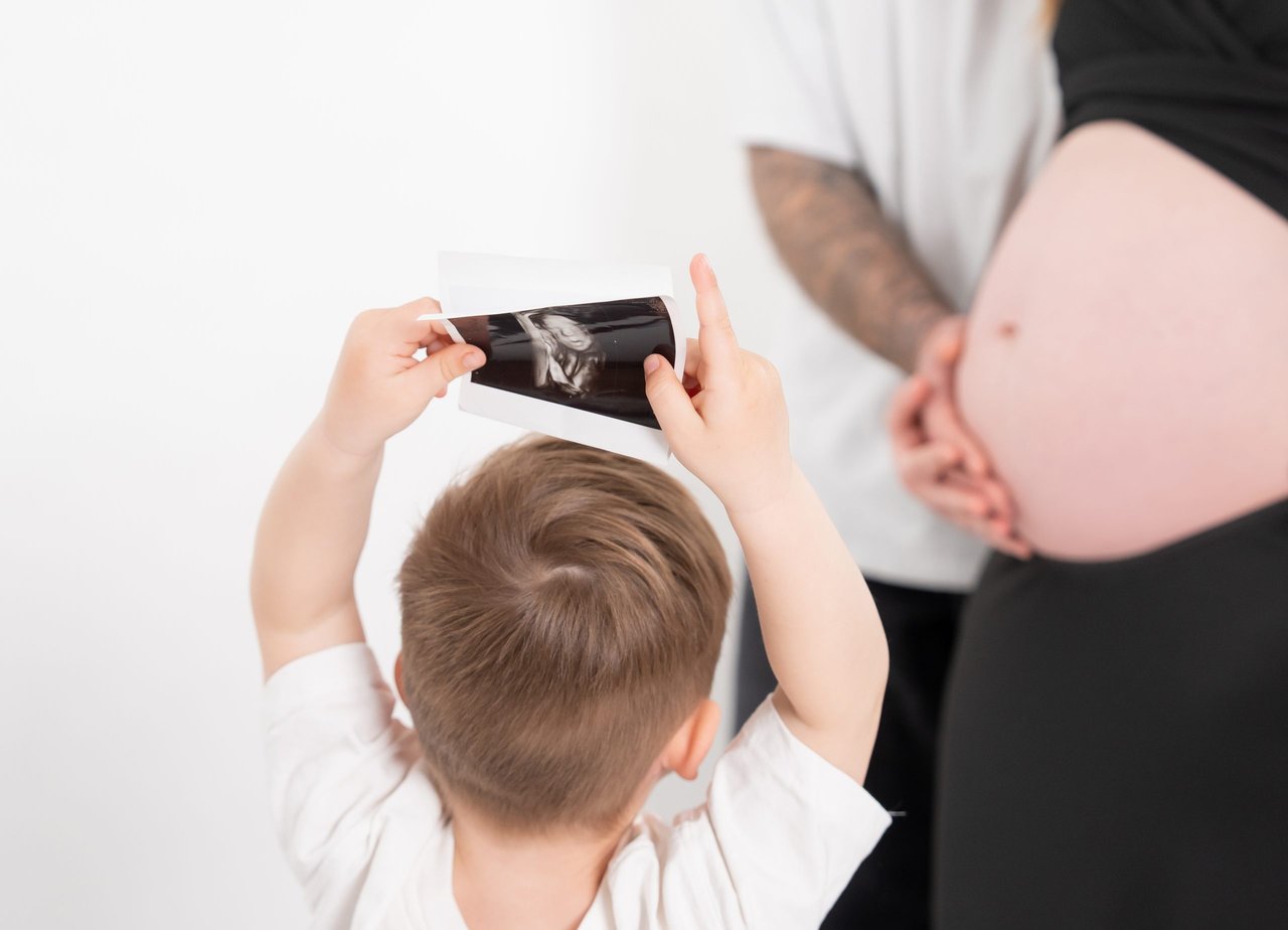 Babybauch-Shooting: Kind haelt Ultraschallbild an Bauch, quer – Photography Ruel, Ebreichsdorf